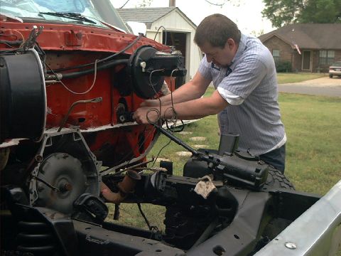 1978 Ford Bronco - Mechanic works on the engine bay of a vehicle, focusing on the transmission and brake system.