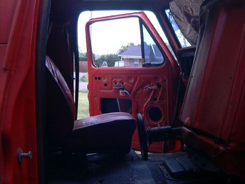 1978 Ford Bronco - Interior view of a red vehicle with the driver's side door open, revealing the inner workings of the door panel and the seat.