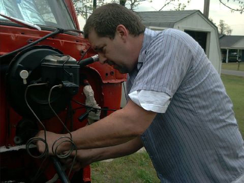 1978 Ford Bronco - Mechanic works on brake system components in the engine bay of a red vehicle.