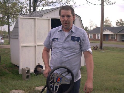 1978 Ford Bronco - Man in GRT shirt holds steering wheel and drive shaft in front of a shed.