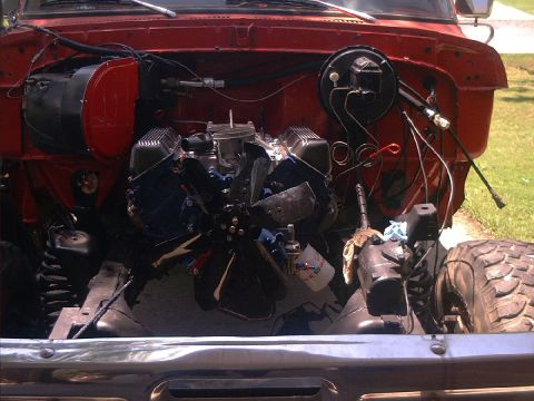 1978 Ford Bronco - The engine bay of a red truck is shown with the engine partially disassembled and the front suspension visible.