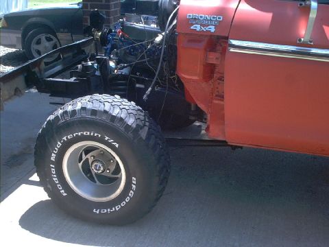 1978 Ford Bronco - An orange 1978 Ford Bronco Ranger 4x4 is partially disassembled, showing its engine and a large tire.