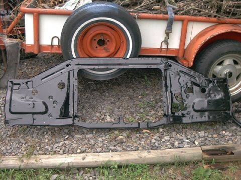 1978 Ford Bronco - A black metal radiator support frame is laid out on gravel in front of a trailer with a spare tire.