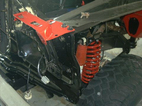 1978 Ford Bronco - The front suspension and frame components of a vehicle are visible, red coil springs and shocks.