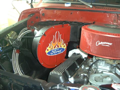 1978 Ford Bronco - Close-up of a red Ford engine bay, showing a custom fan shroud with flames and an Outlaw air filter.