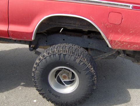 1978 Ford Bronco - The rear wheel and suspension of a red pickup truck are shown in this close-up side view.