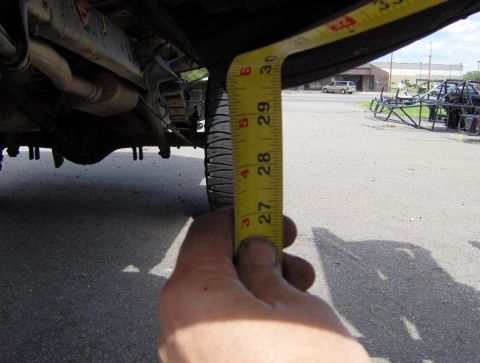 1978 Ford Bronco - A tape measure is held up to the undercarriage of a vehicle, indicating a measurement.