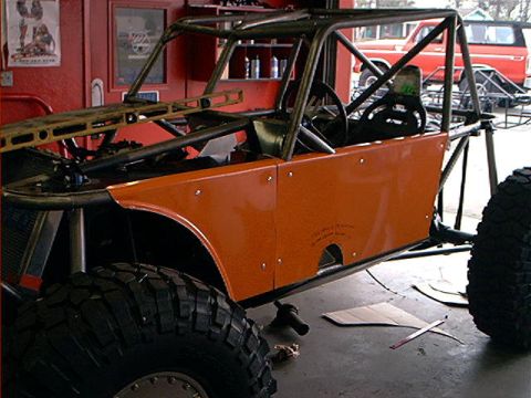 1978 Ford Bronco - An orange rockcrawler project vehicle is shown in a garage, with a red truck visible in the background.