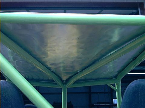 1978 Ford Bronco - The interior of a vehicle shows a custom green roll cage with brushed metal panels overhead.
