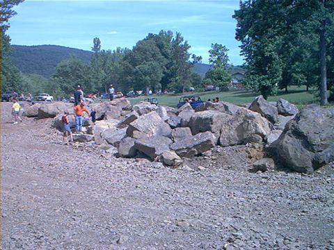 1978 Ford Bronco - People and off-road vehicles are seen in a rocky outdoor area with trees and hills in the background.