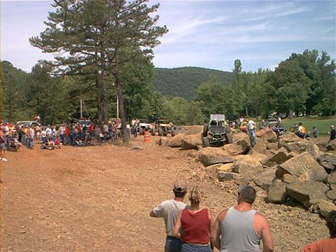 1978 Ford Bronco - A group of people watch as off-road vehicles tackle a challenging rock obstacle course on a sunny day.