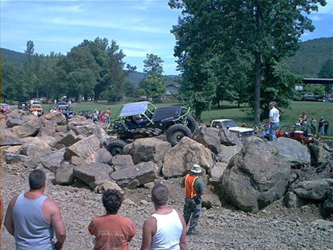 1978 Ford Bronco - A custom-built rock crawler vehicle with solar panels on its roof attempts to traverse a challenging course made of large boulders.