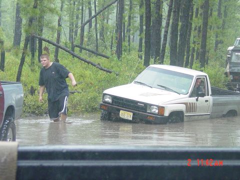 1995 Dodge 1500 - A person walks through water near a white Toyota pickup truck that appears to be stuck in a flooded area.