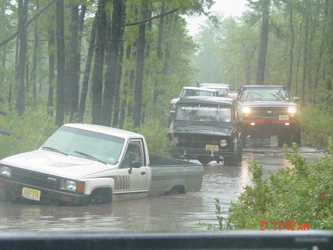 1995 Dodge 1500 - Several off-road vehicles navigate a flooded dirt road through a wooded area.