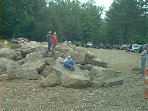 1978 Ford Bronco - A group of off-road vehicles are parked in a lot while people navigate a rocky terrain.