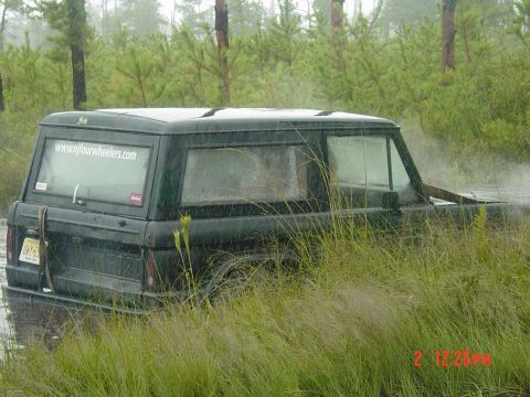 1995 Dodge 1500 - SUV stuck in water and grass, with a website visible on the rear window.