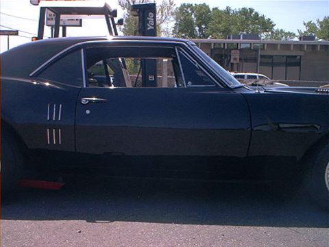 1978 Ford Bronco - A dark-colored coupe with distinctive triple vents on the front fender is parked outdoors.