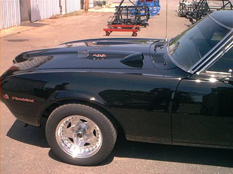 1978 Ford Bronco - A close-up of a black muscle car's fender and hood, showing a hood scoop and custom wheels.