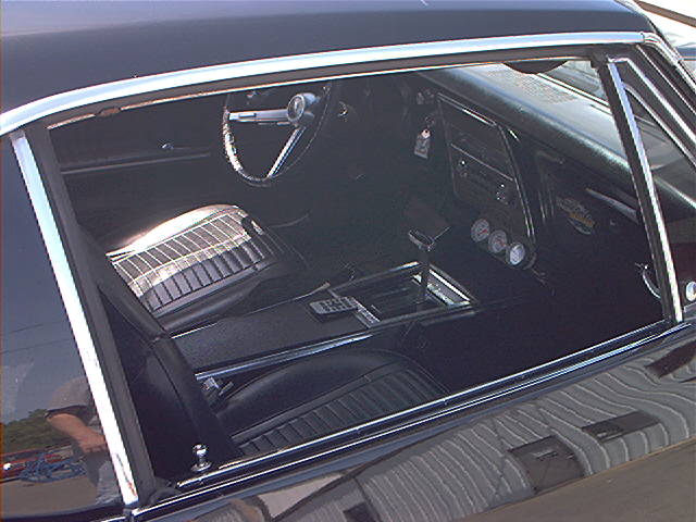 Interior shot of a classic car, showing the steering wheel, dashboard with gauges, center console with shifter, and front seats