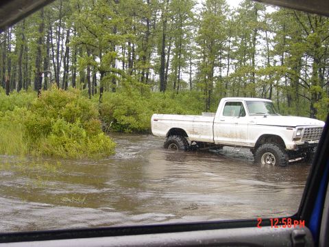 1995 Dodge 1500 - A white pickup truck navigates through a flooded wooded area, its tires submerged in the water.