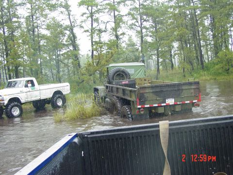 1995 Dodge 1500 - A camouflaged military truck navigates through a flooded wooded area, with a white pickup truck visible in the background.