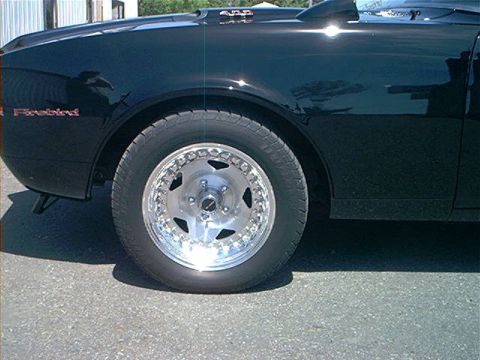 1978 Ford Bronco - Close-up of a black car's front fender and wheel, with a 'Firebird' emblem visible.