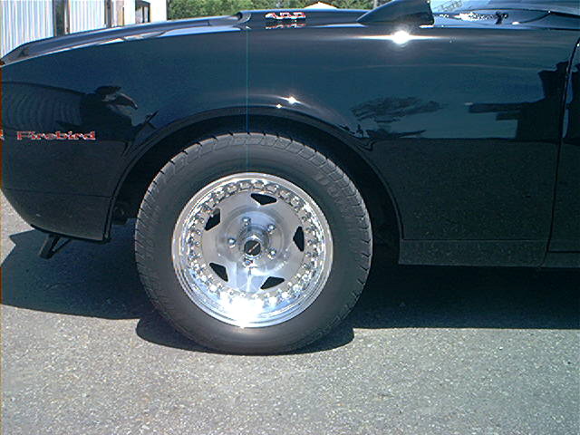 Black car fender with 'Firebird' emblem, showing a polished five-spoke wheel and tire