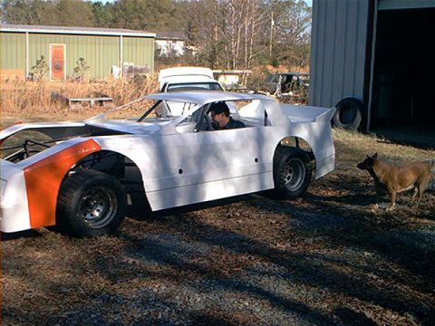 1978 Ford Bronco - A white race car with an orange fender sits outside a garage, with a dog nearby.