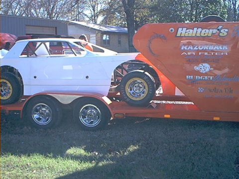 1978 Ford Bronco - A white race car is transported on an orange trailer that displays various advertisements and sponsor logos.