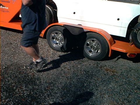 1978 Ford Bronco - Trailer carrying a white car, with a person standing nearby. The trailer has dual wheels.