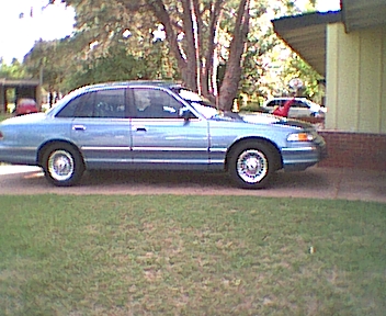 1994 Ford Crown Victoria - Side view of a blue 1994 Ford Crown Victoria sedan parked on a grassy lawn.