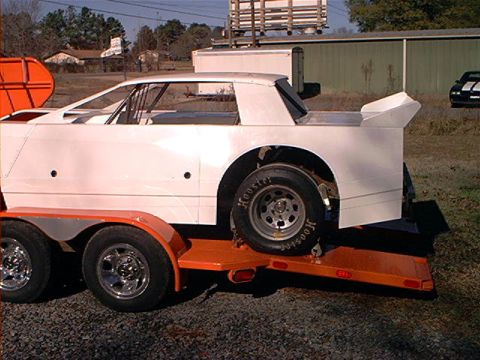 1978 Ford Bronco - A white race car body is loaded onto an orange trailer, ready for transport.