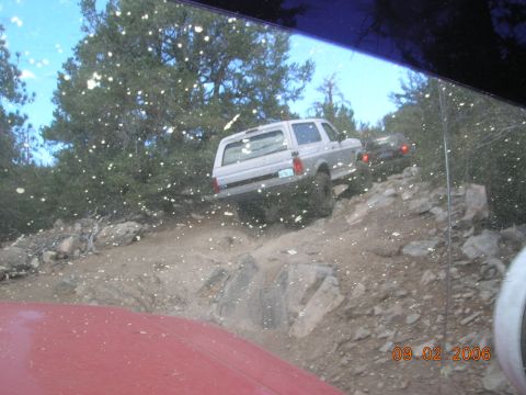 1985 Ford Bronco - A silver SUV navigates a challenging rocky trail, with another vehicle visible behind it.