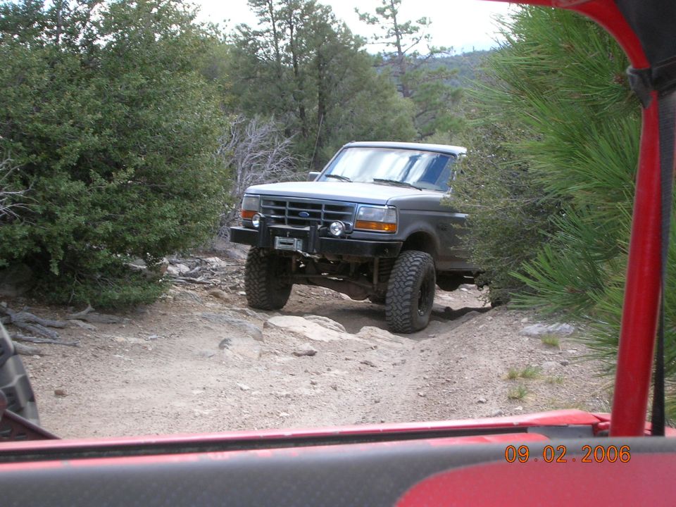 Gray Ford Bronco with aftermarket bumper and winch driving on a rocky dirt trail, seen from another vehicle