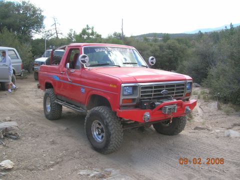1985 Ford Bronco - A red Ford Bronco is parked on a dirt path with trees and hills in the background. The date 09.02.2006 is visible.