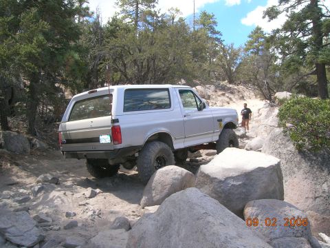 1985 Ford Bronco - This silver SUV, likely a 1992 Ford Bronco, is shown off-roading on a challenging rocky path.