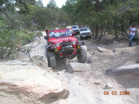 1985 Ford Bronco - Several off-road vehicles traverse a challenging rocky path on a sunny day.