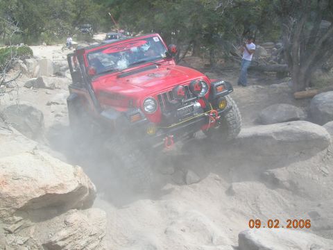 1985 Ford Bronco - A red Jeep Wrangler tackles a challenging off-road course, demonstrating its capability on rough terrain.