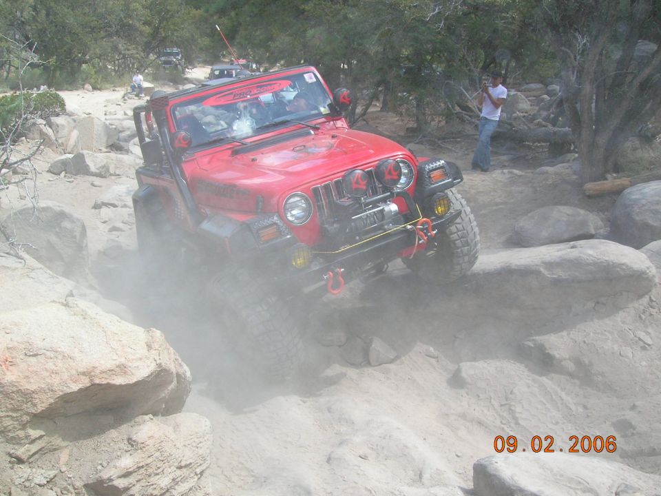 Red Jeep Wrangler navigating rocky terrain, kicking up dust