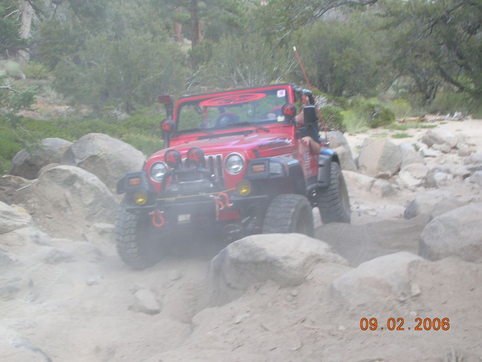 Red Jeep Wrangler navigating a boulder-strewn dirt path. Date stamp reads 09.02.2006