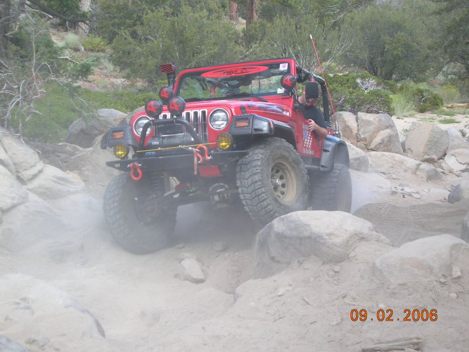 red Jeep Wrangler climbing over rocks on a dirt trail