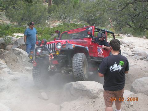 1985 Ford Bronco - A red Jeep Wrangler tackles a challenging off-road course, with onlookers observing the action.
