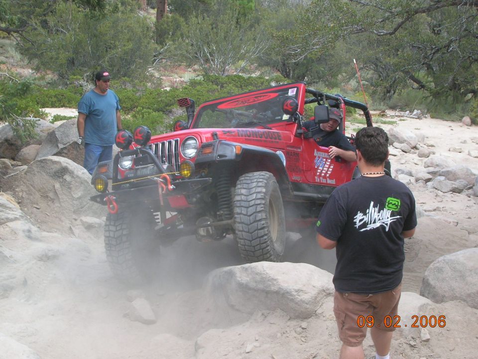 Red Jeep Wrangler navigating rocky terrain, kicking up dust