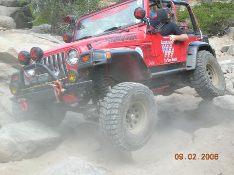 1985 Ford Bronco - Red Jeep Wrangler navigating rocky terrain, kicking up dust.