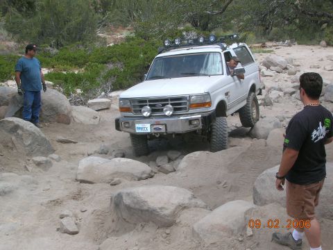 1985 Ford Bronco - A white Ford Bronco is shown off-roading on a rocky trail with two men observing the vehicle.