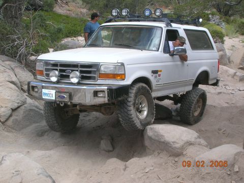 1985 Ford Bronco - This white Ford Bronco is equipped for off-road adventures, with a lifted suspension and large tires tackling a rocky path.
