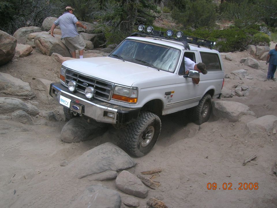 White Ford Bronco navigating rocky terrain, front bumper visible with license plate reading "BROOCK"