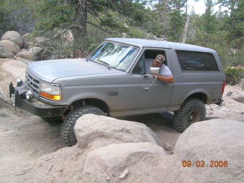 1985 Ford Bronco - A gray Ford Bronco navigates a rocky trail with a driver inside.