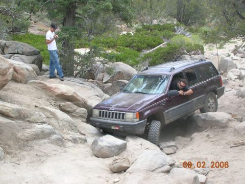 1985 Ford Bronco - A maroon Jeep Grand Cherokee navigates a challenging rocky trail on a sunny day.