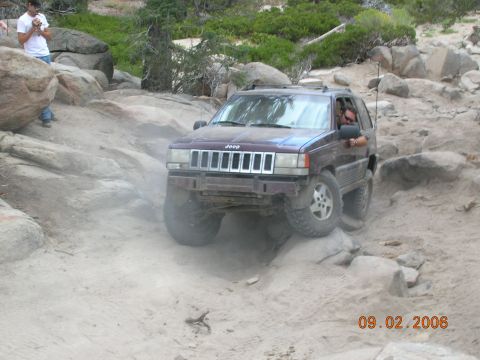 1985 Ford Bronco - A Jeep Grand Cherokee navigates a challenging rocky terrain on a sunny day.